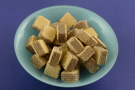 Bite size chocolate hazelnut wafer cookies in blue bowl on blue backgroundの写真素材