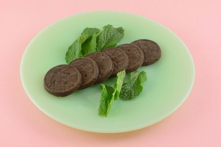 Fudge mint cookies with fresh mint leaves on green plate on pink backgroundの写真素材