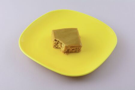 Toffee flapjack square cake bar with bite missing on yellow plate on lavender backgroundの写真素材