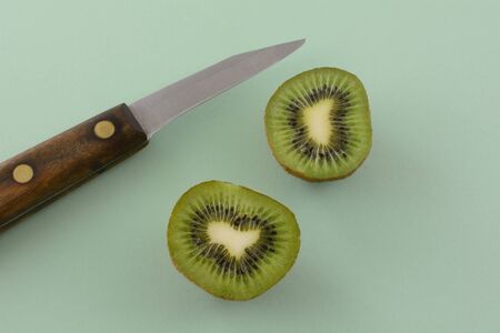 Kiwi fruit halves and kitchen knife on light green backgroundの写真素材