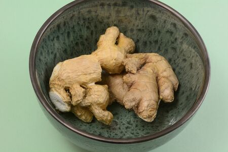 Raw ginger root spice in green bowl on light green backgroundの写真素材