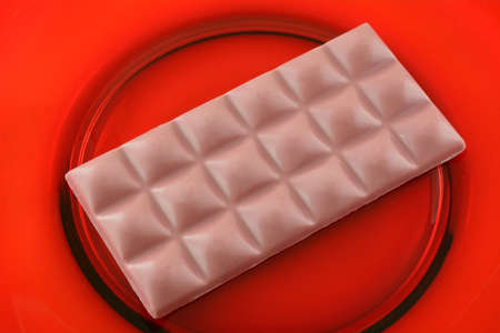 Closeup of ruby chocolate cacao snack bar on red glass plate