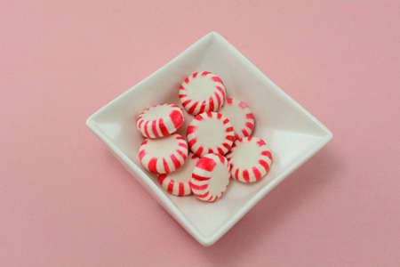 Peppermint hard candy in white candy dish on pink backgroundの写真素材