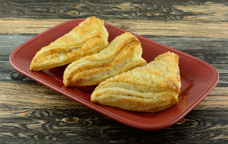 Three apple turnovers breakfast pastries on red platter on table