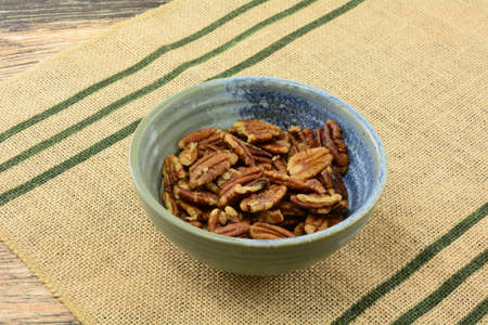 Roasted pecan nut halves and pieces on ceramic bowl on place mat