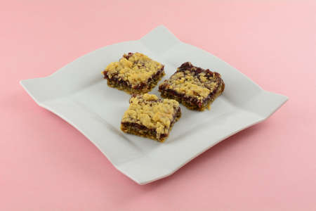 Three baked raspberry oat crumble squares on white dessert plate on pink backgroundの写真素材