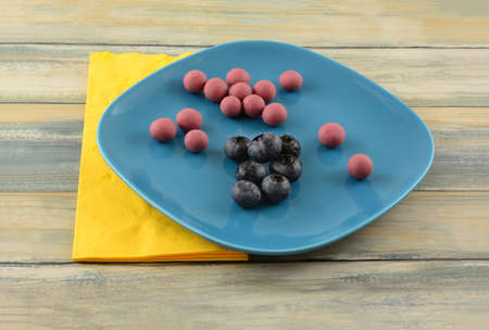 Blueberries dipped in ruby cacao chocolate and fresh raw blueberries on blue snack plate with yellow...
