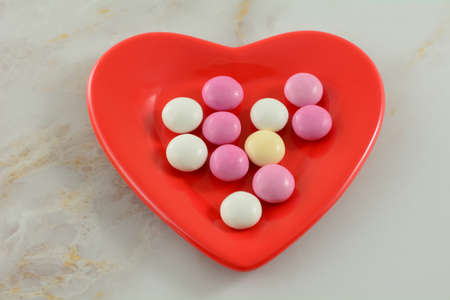 Pink, white and yellow Valentine's Day candy covered chocolate pieces on red heart shaped plate on...