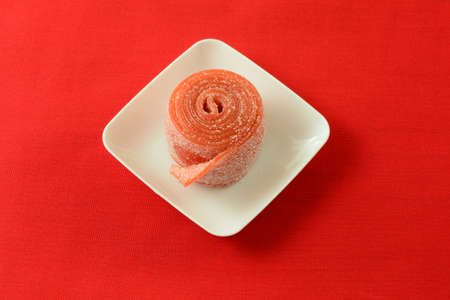 Sour strawberry fruit roll up candy in white candy dish on red backgroundの写真素材