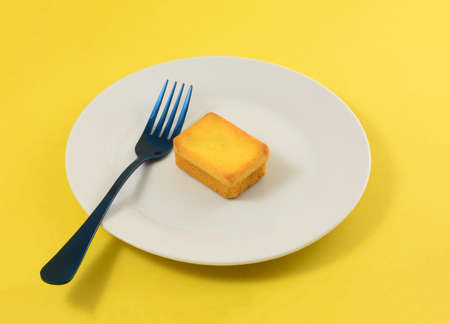 Yuzu sponge cake snack in white plate with fork on yellow background