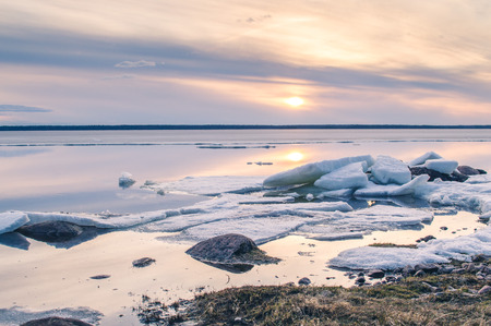 The abstract image of the sunset at the lake with the melting ice in early spring. Golden hour colors, grass and stones.の写真素材