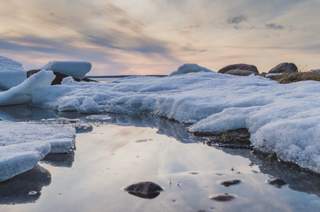 Sunset winter lake shore with stones, snow and ice. Closeup, Ladoga lake, selective focusの写真素材