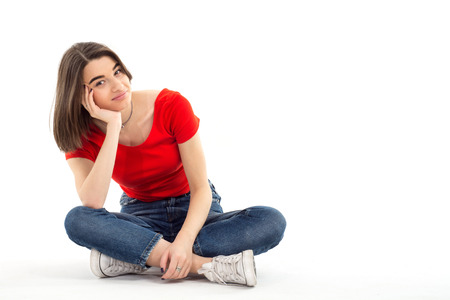 Portrait of a beautiful young girl wearing red t-shirt sitting on the floor, legs crossed against...