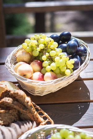 Closeup of basket with fruits: grapes, peaches and plums on a wooden table, outdoor party or picnicの写真素材