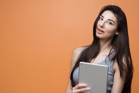Closeup portrait of a young brunette girl with tablet in her hand smiling and looking in the camera....