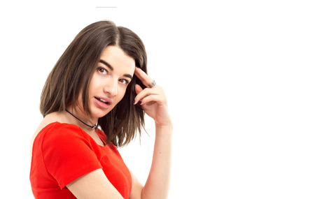 closeup portrait of a young brunette girl in red t-shirt looking suspiciously and thinking into the camera against white background.の写真素材