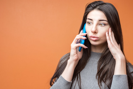 Pretty modern woman in gray having phone call looking amazed with news standing on orange background