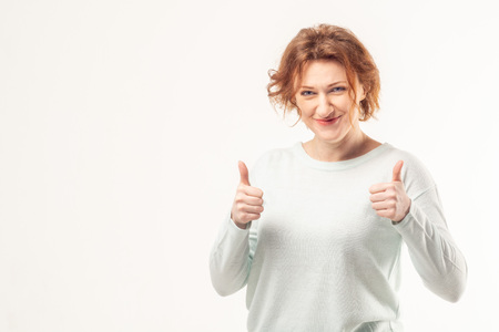 Confident successful mature red haired woman showing thumbs up gesture with a happy smile on her face against white backgroundの写真素材
