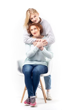 Young teenage girl embracing beautiful  red haired woman on chair standing on white backgroundの写真素材