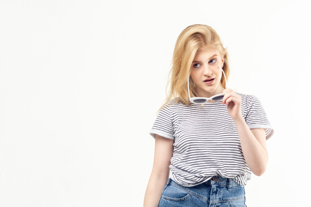 Young blonde pretty teenage girl in striped t-shirt and denim holding sunglasses and looking to the...