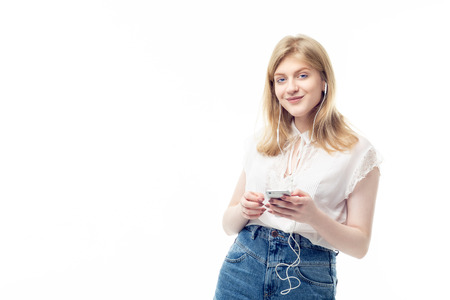 Young beautiful teenage girl with blonde hair listening to the music with headphones on her smartphone and smiling to the camera. Lifestyle, technology and people conceptの写真素材