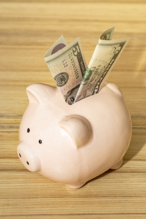 Pink piggy bank with five dollar bill on wooden background. Money, savings and investments conceptの写真素材