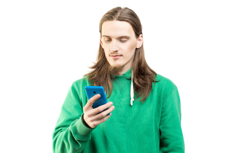 Portrait of young handsome man in green hoodie looking at the mobile phone in his hand agains white background. Lifestyle, people and technology conceptの写真素材