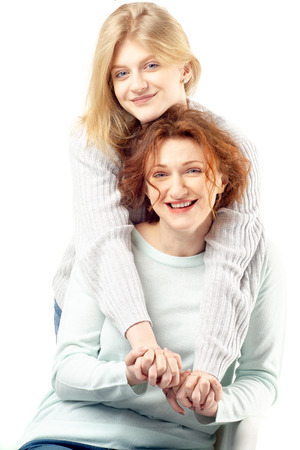 Young blonde teenage girl embracing beautiful happy smiling red haired woman on chair standing on white backgroundの写真素材