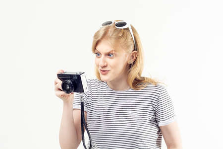 Pretty blonde teenage girl in striped t-shirt looking at the vintage camera in her hands with curious and surprised expression on her faceの写真素材
