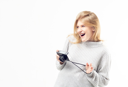 Pretty blonde teenage girl in a bright sweater holding vintage camera in her hands and laughingの写真素材