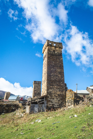 Picturesque landscape of aged Georgian rural community Ushguli with Typical Svaneti defensive tower houses in valley of beautiful mountains with snowy peaks and cloudy blue sky.の写真素材