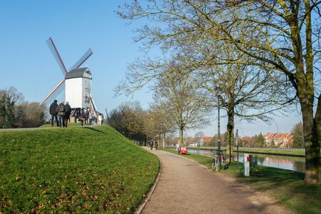 Brugge, West Flanders,  Belgium - December 2018: Bonne-Chiremolen windmill on a sunny day with green grass and clear blue sky,  people walking aroundのeditorial素材