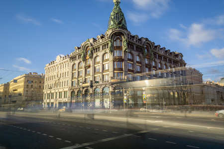 Blurred trails of cars on road near amazing old building against cloudy blue sky in beautiful city. Singer building, Saint-Petersburgの写真素材