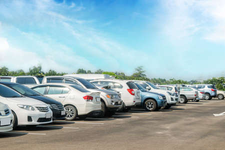 Car parked in large asphalt parking lot with trees, white cloud, blue sky background. Outdoor parking lot with fresh ozone and green environment of travel transportation conceptの写真素材