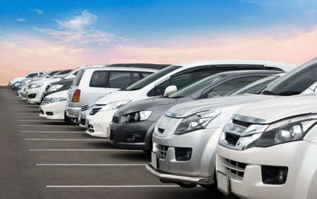 Cars parked in asphalt parking lot in a row with blue sky background. Outdoor parking lot with fresh...