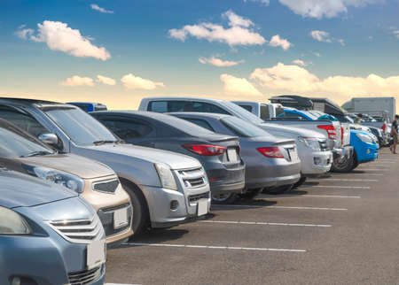 Car parking in large asphalt parking lot with white cloud and blue sky background. Outdoor parking...