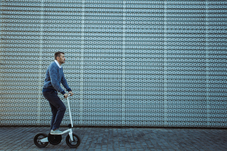 Side view of man pushing kick scooter while riding on beautiful embankmentの写真素材
