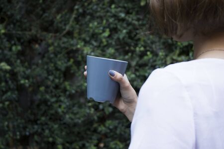 Mockup of female hand holding a coffee cup on natural garden background.の写真素材