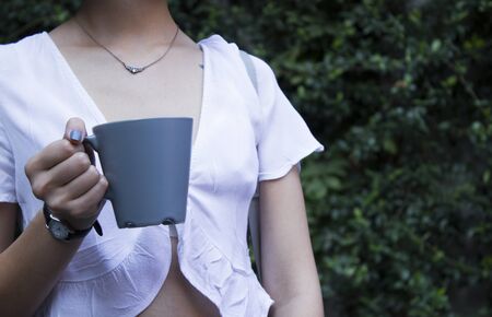 Mockup of female hand holding a coffee cup on natural garden background.の写真素材