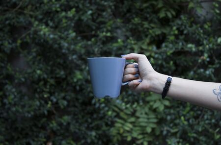 Mockup of female hand holding a coffee cup on natural garden background.の写真素材