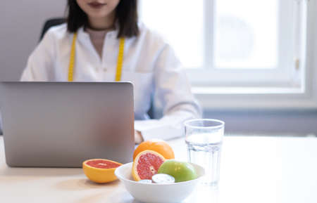 dietitian woman working with her computer and an office with mixed fruit and water on the tableの写真素材