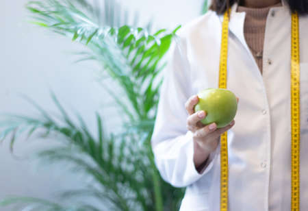 female dietitian in apron and tape measure holding appleの写真素材