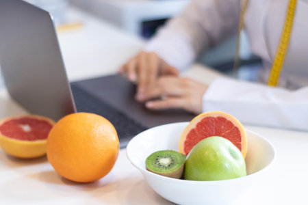 dietitian woman working with her computer and an office with mixed fruit and water on the tableの写真素材