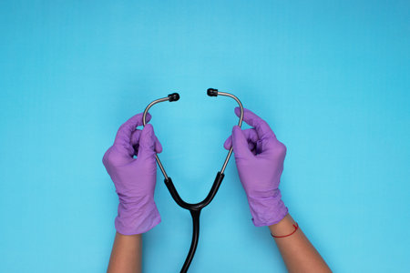 hands holding stethoscope with lilac colored medical gloves on light blue backgroundの写真素材