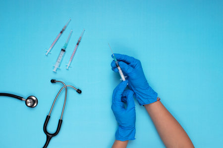 needle, stethoscope and other needles held in blue gloved hand on light blue backgroundの写真素材