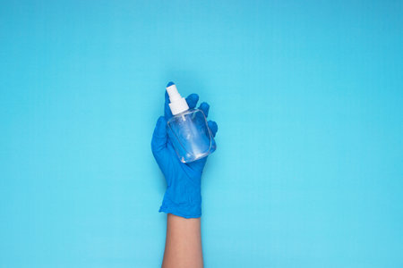 hand holding disinfectant spray with blue medical gloves on light blue backgroundの写真素材