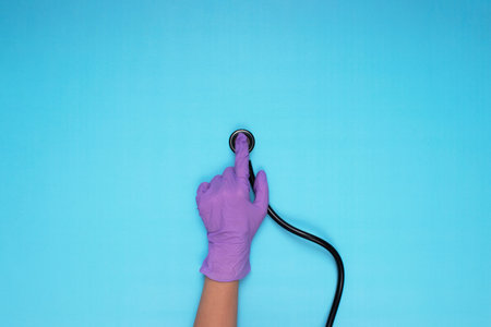 hands holding stethoscope with lilac colored medical gloves on light blue backgroundの写真素材