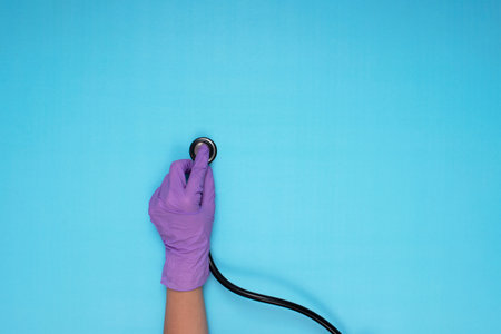 hands holding stethoscope with lilac colored medical gloves on light blue backgroundの写真素材