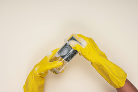 woman wearing yellow cleaning gloves on light color background cleaning glass cup with cleaning spongeの写真素材