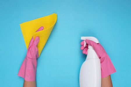 Woman wearing pink cleaning gloves on a light blue background, holding a cleaning spray and a cleaning clothの写真素材